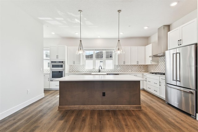 kitchen featuring dark wood-style floors, stainless steel appliances, wall chimney exhaust hood, tasteful backsplash, and a center island