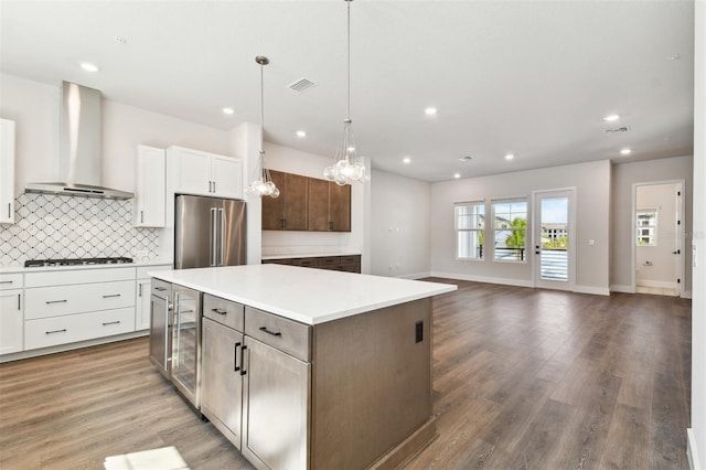 kitchen with visible vents, backsplash, wall chimney range hood, high quality fridge, and wood finished floors