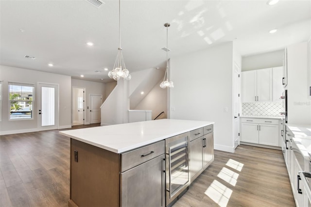 kitchen with tasteful backsplash, a center island, wine cooler, wood finished floors, and white cabinetry