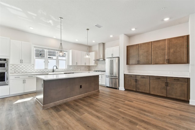 kitchen with visible vents, white cabinetry, stainless steel appliances, wall chimney exhaust hood, and light countertops