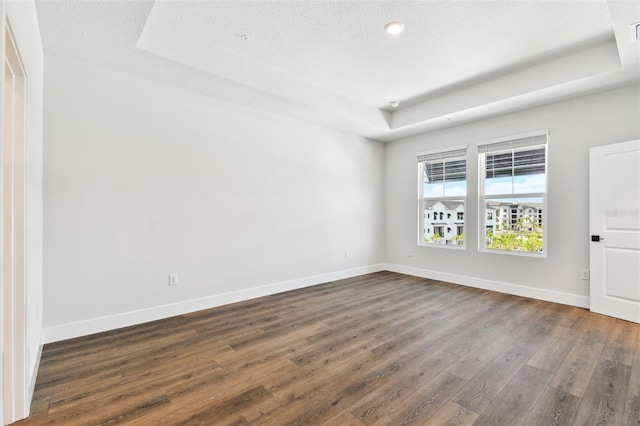 spare room with a raised ceiling, baseboards, and dark wood-style flooring