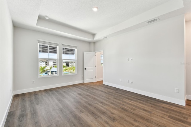 unfurnished room with a tray ceiling, dark wood-style floors, visible vents, and baseboards