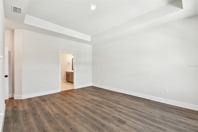 unfurnished room with visible vents, a tray ceiling, dark wood-type flooring, and baseboards