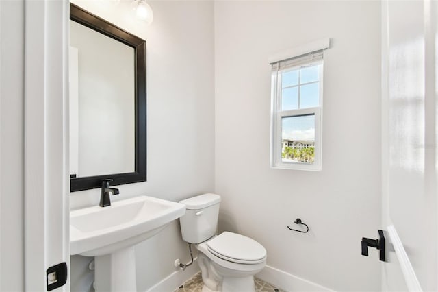 half bath featuring baseboards and toilet