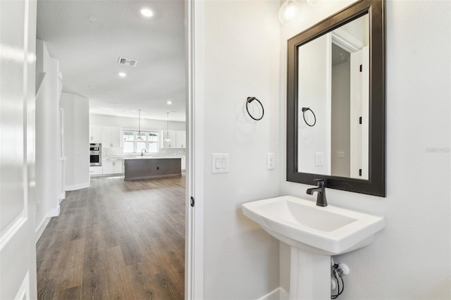 bathroom featuring wood finished floors, visible vents, backsplash, and baseboards