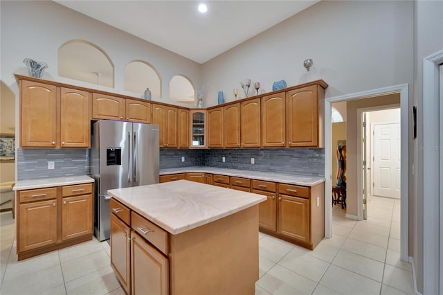 kitchen featuring stainless steel refrigerator with ice dispenser, decorative backsplash, high vaulted ceiling, a kitchen island, and light tile patterned flooring