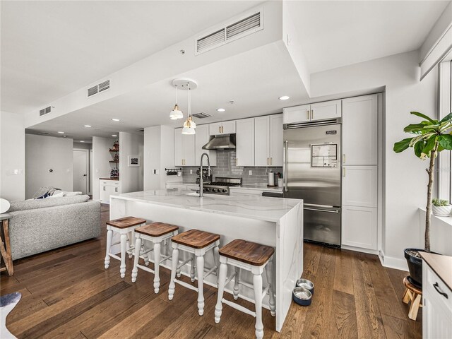 kitchen featuring decorative light fixtures, tasteful backsplash, built in refrigerator, light stone counters, and dark wood-type flooring