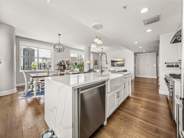 kitchen featuring appliances with stainless steel finishes, dark wood-type flooring, light stone countertops, an island with sink, and pendant lighting