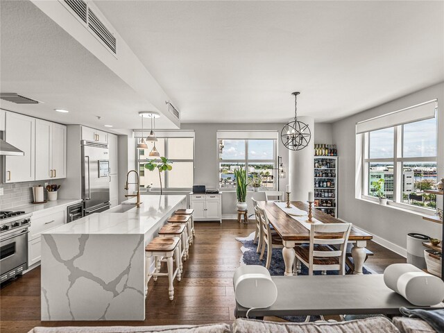 kitchen featuring a kitchen island with sink, appliances with stainless steel finishes, light stone counters, and dark hardwood / wood-style flooring