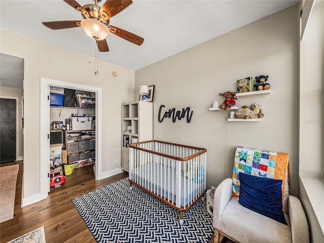 bedroom featuring ceiling fan, a crib, and dark wood-type flooring