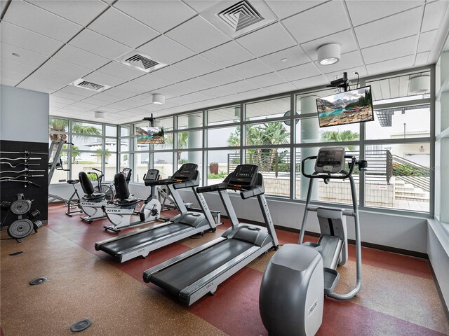 exercise room with a paneled ceiling and a healthy amount of sunlight