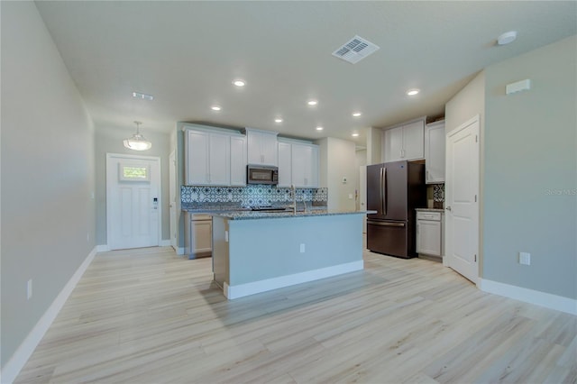 kitchen featuring decorative backsplash, an island with sink, stone countertops, appliances with stainless steel finishes, and light hardwood / wood-style floors