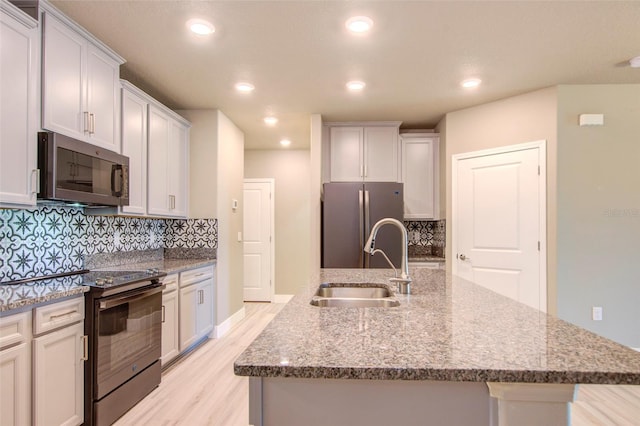 kitchen with tasteful backsplash, white cabinets, appliances with stainless steel finishes, light hardwood / wood-style floors, and sink