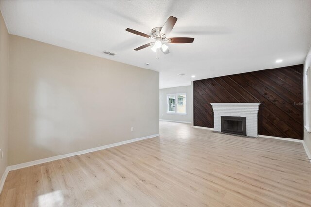 unfurnished living room featuring a fireplace, light wood-type flooring, ceiling fan, and wood walls