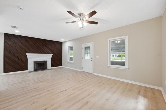 unfurnished living room featuring ceiling fan, a fireplace, wooden walls, and light hardwood / wood-style flooring