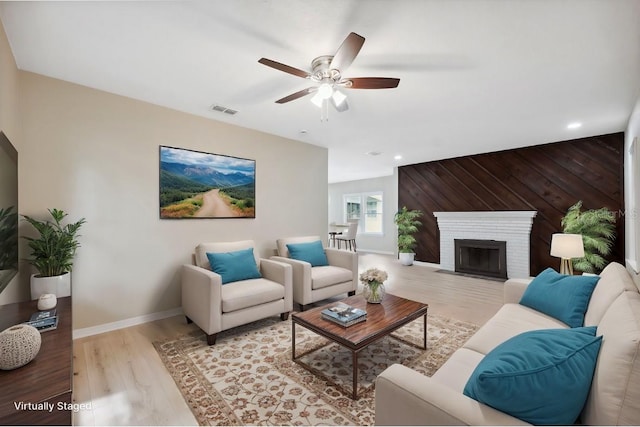 living room with light hardwood / wood-style floors, a brick fireplace, ceiling fan, and wood walls