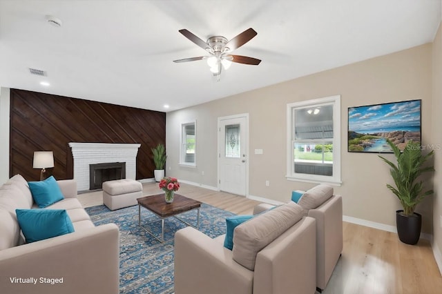 living room with wood walls, ceiling fan, light hardwood / wood-style floors, and a brick fireplace