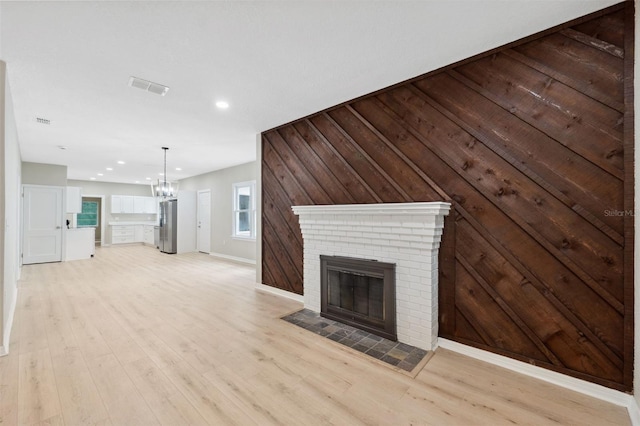 unfurnished living room featuring light hardwood / wood-style floors, a fireplace, wooden walls, and an inviting chandelier