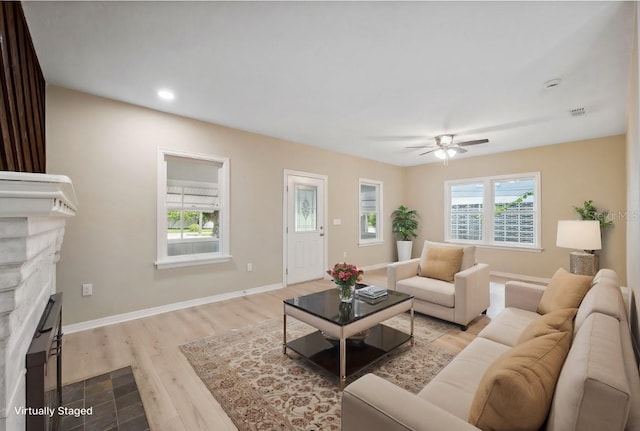 living room with ceiling fan, a stone fireplace, and light hardwood / wood-style flooring