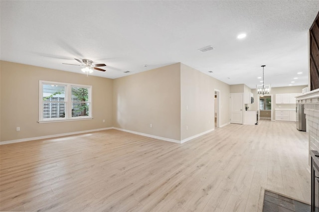 unfurnished living room featuring a fireplace, a textured ceiling, ceiling fan with notable chandelier, and light hardwood / wood-style flooring