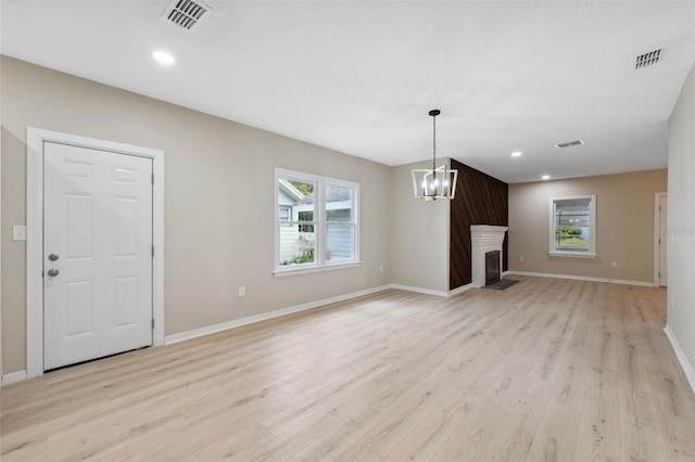 unfurnished living room featuring a large fireplace, an inviting chandelier, and light hardwood / wood-style flooring