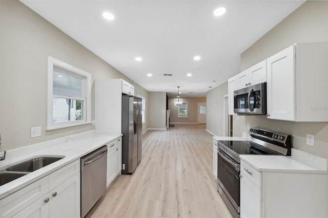 kitchen featuring white cabinets, stainless steel appliances, decorative light fixtures, and light wood-type flooring