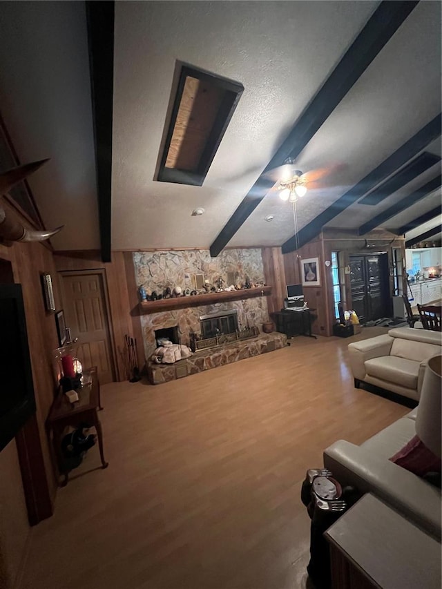 living room featuring lofted ceiling with beams, ceiling fan, a fireplace, wood walls, and wood-type flooring