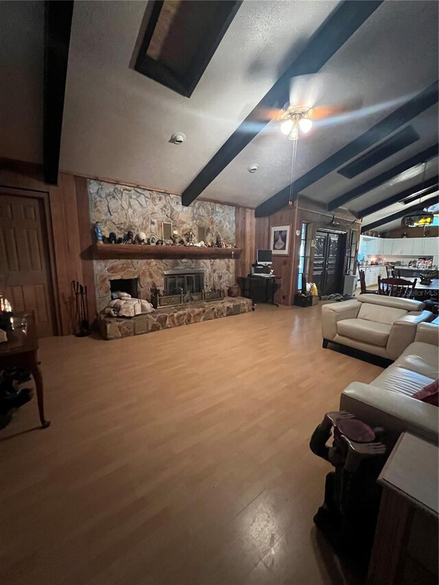 living room featuring hardwood / wood-style floors, ceiling fan, wood walls, a fireplace, and vaulted ceiling with beams