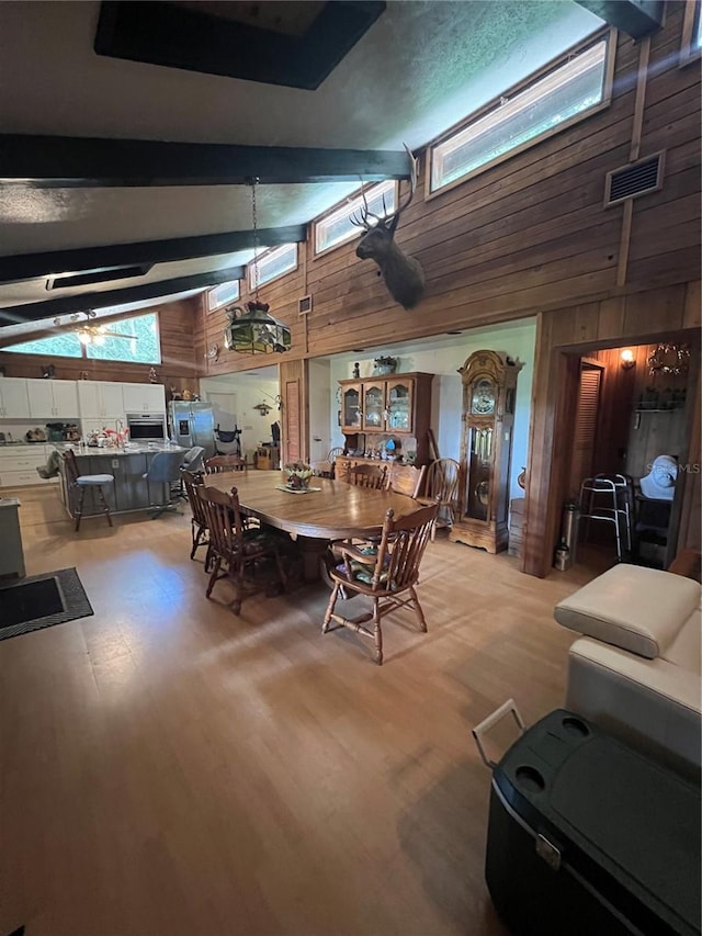 dining room with beamed ceiling, wooden walls, hardwood / wood-style flooring, and high vaulted ceiling