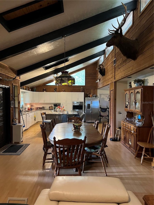 dining room featuring beamed ceiling, wood walls, sink, and high vaulted ceiling