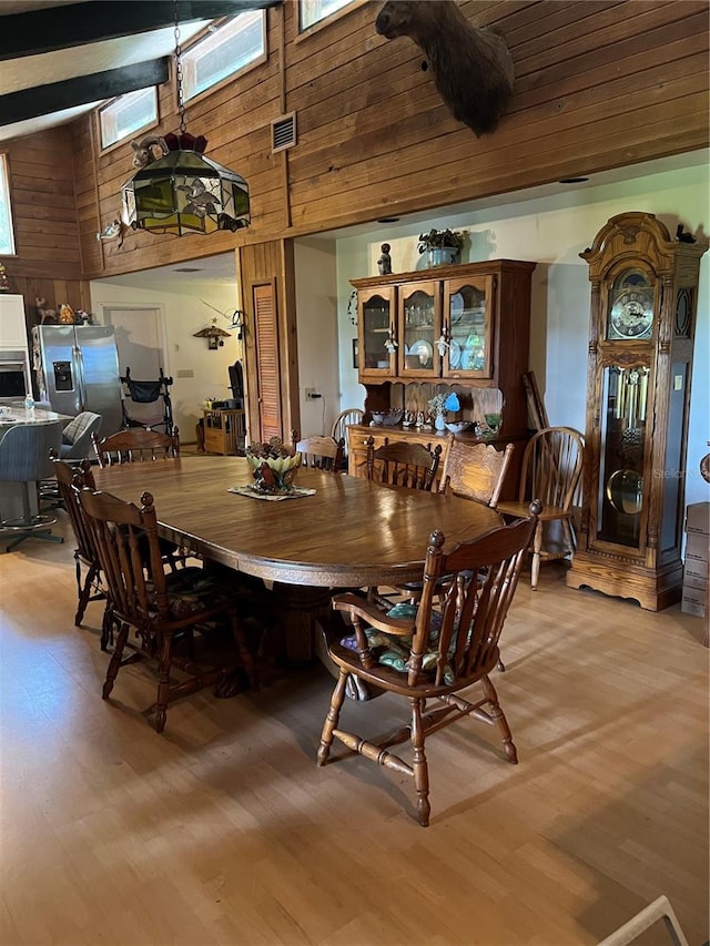 dining space featuring wood walls, high vaulted ceiling, light wood-type flooring, and a skylight