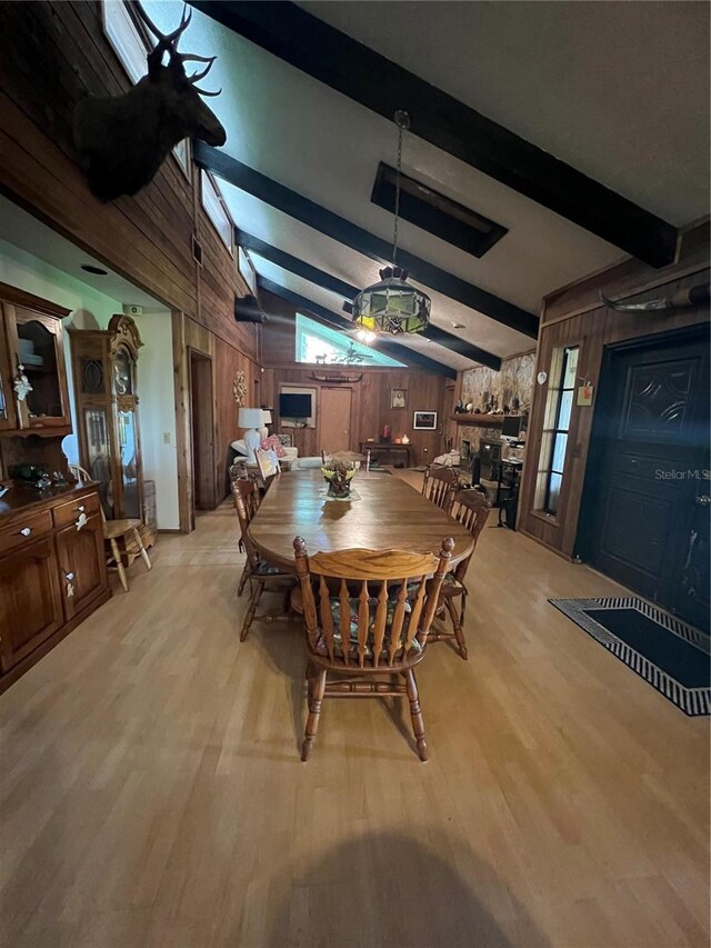 dining room with light wood-type flooring, wood walls, and vaulted ceiling with beams