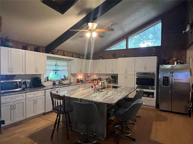 kitchen with lofted ceiling, appliances with stainless steel finishes, white cabinets, a kitchen island, and ceiling fan