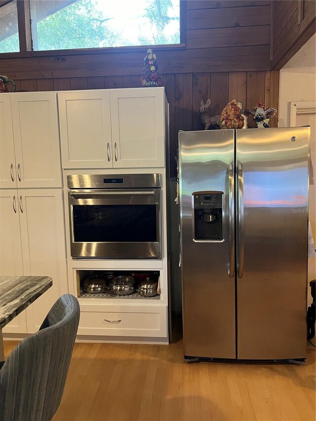 kitchen featuring light hardwood / wood-style flooring, appliances with stainless steel finishes, white cabinets, and wood walls