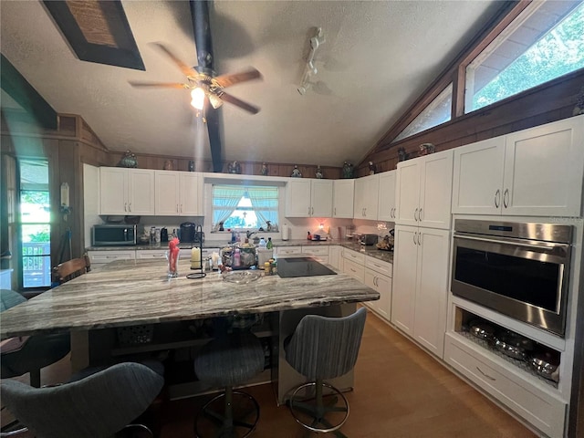 kitchen with a large island, ceiling fan, lofted ceiling, white cabinets, and stainless steel appliances