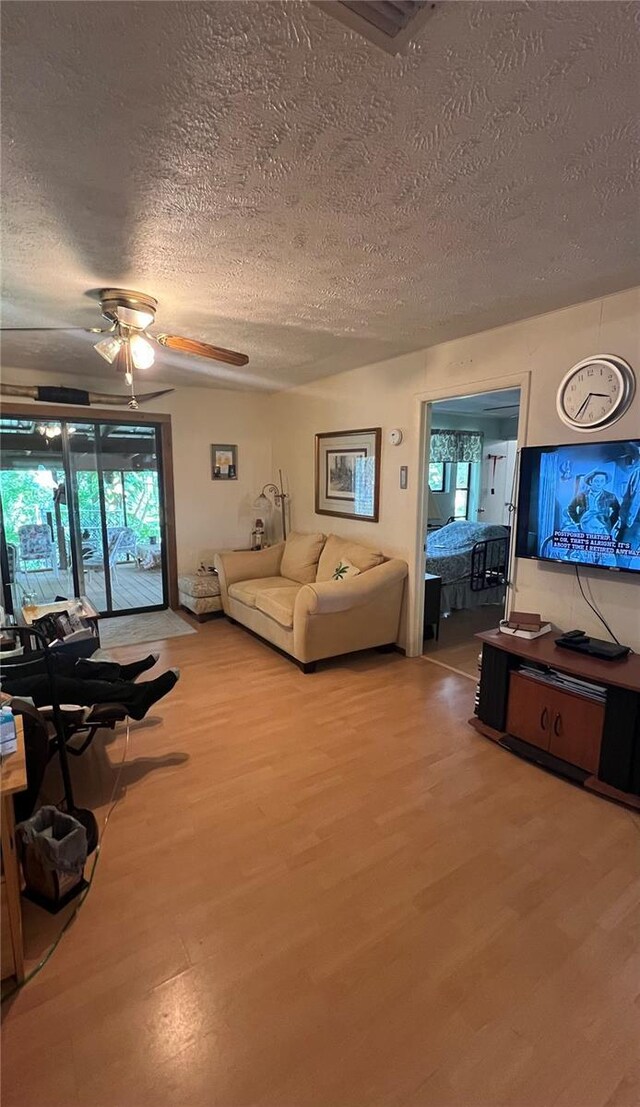 living room with ceiling fan, a textured ceiling, and light hardwood / wood-style floors