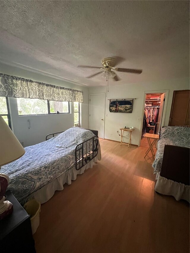 bedroom featuring a textured ceiling, ceiling fan, a spacious closet, a closet, and wood-type flooring