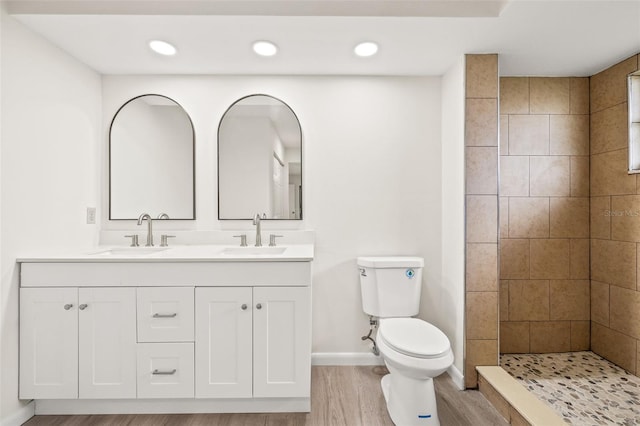 bathroom with tiled shower, hardwood / wood-style flooring, dual vanity, and toilet