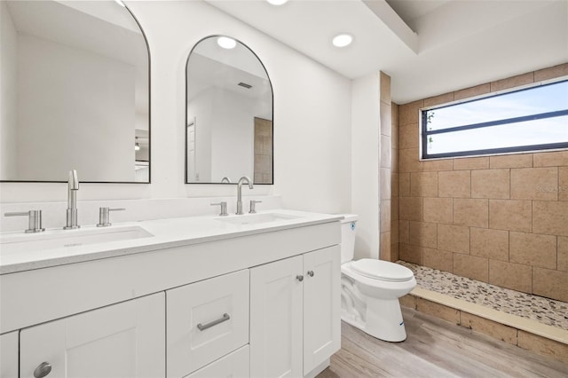 bathroom with hardwood / wood-style floors, dual bowl vanity, a tile shower, and toilet