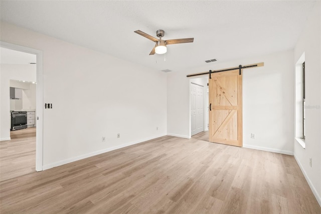 unfurnished bedroom with ceiling fan, a barn door, and light hardwood / wood-style flooring