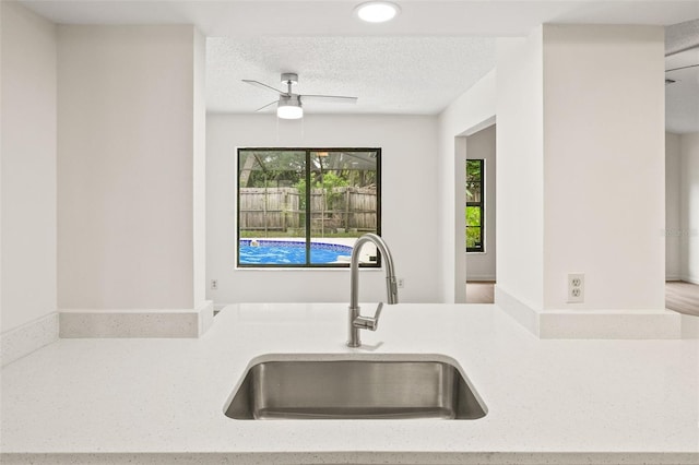 kitchen featuring a textured ceiling, light stone countertops, ceiling fan, sink, and hardwood / wood-style flooring