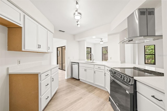 kitchen featuring electric range, track lighting, wall chimney range hood, and white cabinetry