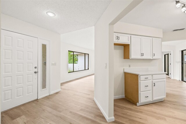 kitchen with light wood-type flooring, rail lighting, a textured ceiling, and white cabinetry