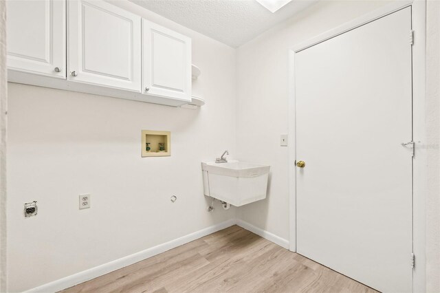 clothes washing area with hookup for a washing machine, a textured ceiling, cabinets, hookup for an electric dryer, and light hardwood / wood-style floors