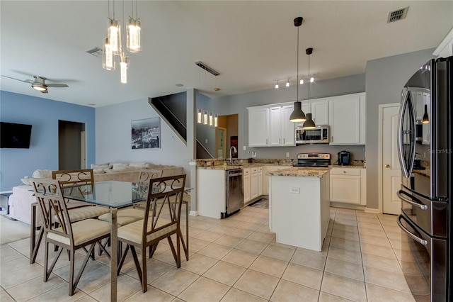 kitchen featuring appliances with stainless steel finishes, a kitchen island, white cabinetry, light stone counters, and decorative light fixtures