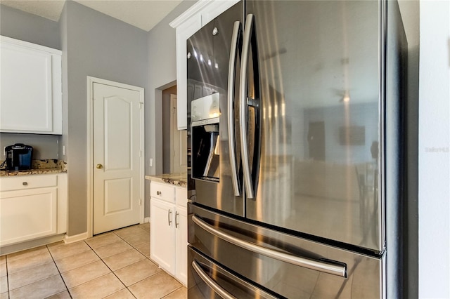 kitchen with stainless steel fridge, white cabinets, and stone countertops