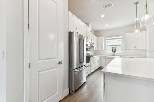 kitchen with white cabinetry, light hardwood / wood-style floors, decorative light fixtures, decorative backsplash, and appliances with stainless steel finishes