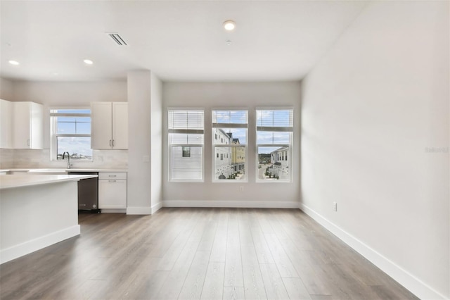 kitchen featuring hardwood / wood-style floors, backsplash, white cabinetry, and stainless steel dishwasher