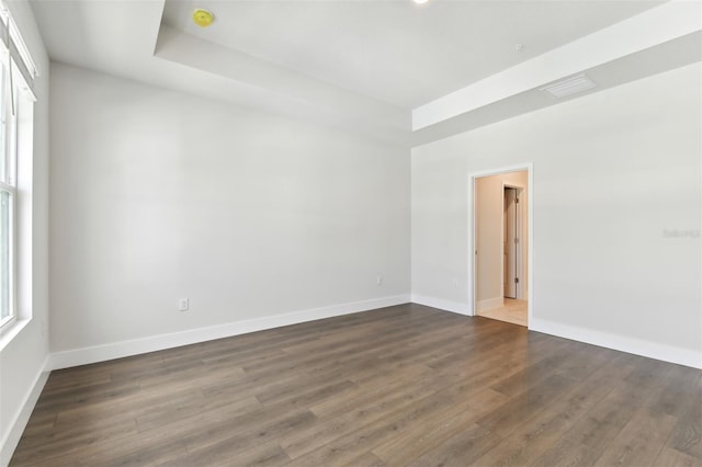 spare room with a tray ceiling and dark wood-type flooring