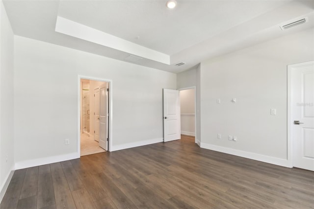 unfurnished bedroom featuring ensuite bathroom, a raised ceiling, and dark wood-type flooring